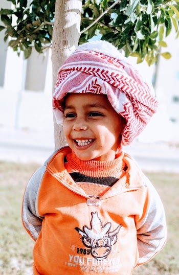 Photo of Smiling Boy in Keffiyeh Standing Near Tree