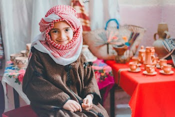 Photo of Smiling Boy in White and Red Keffiyeh Scarf and Brown Jacket Sitting