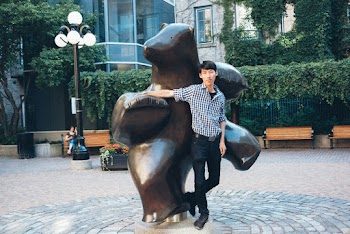 Photo of Smiling Man in White and Black Gingham Shirt Posing By Bear Statue