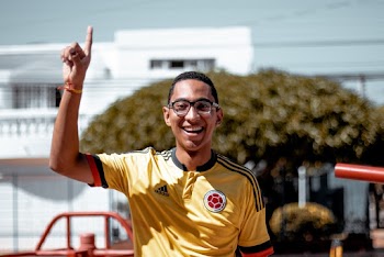 Photo of Smiling Man in Yellow and Black Adidas Jersey Pointing His Hand Up