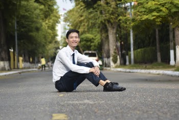 Photo of Smiling Man Sitting in the Middle of the Road During Day