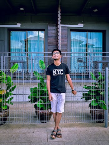 Photo of Smiling Man with His Eyes Closed Standing Beside Black Metal Fence In Front of House