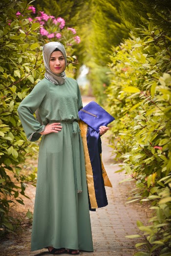 Photo of Smiling Woman Carrying Academic Regalia Standing In Between Green-leafed Plants