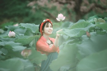 Photo of Smiling Woman Holding a Pink Flower While Sitting in the Middle of a Flower Field