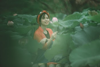 Photo of Smiling Woman Holding a Pink Flower While Sitting in the Middle of a Flower Field