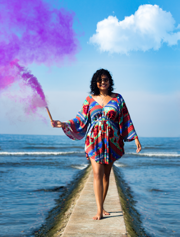 Photo of Smiling Woman Holding Purple Smoke Bomb Walking on Stone Pier
