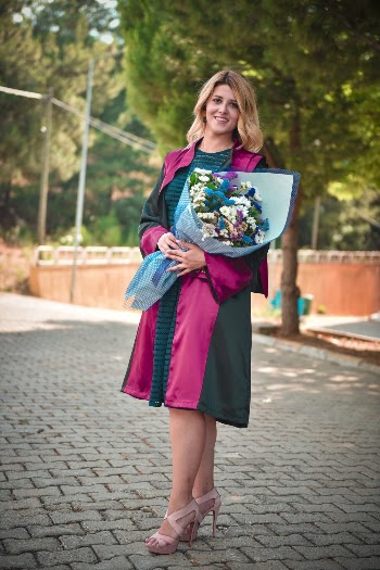 Photo of Smiling Woman in Black and Pink Graduation Gown Posing While Carrying Bouquet of Flowers