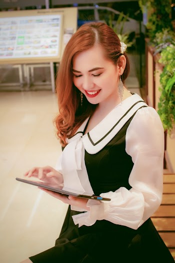 Photo of Smiling Woman in Black and White Outfit Standing While Using a Tablet
