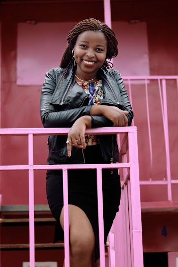 Photo of Smiling Woman in Black Leather Jacket and Black Dress Leaning on Metal Railing Posing