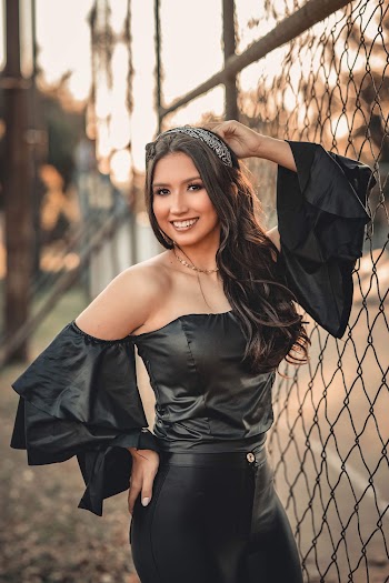 Photo of Smiling Woman in Black Outfit Leaning on Chain-link Fence Posing