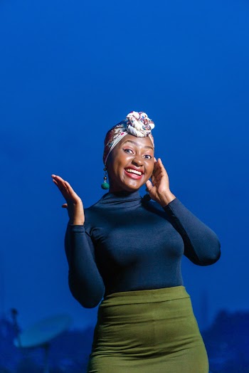 Photo of Smiling Woman in Blue Long-sleeved Fitted Top and Green Skirt Posing Against Blue Background