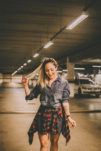 Photo of Smiling Woman in Denim Outfit Holding Her and Looking Down While Walking Alone in Underground Parking Lot