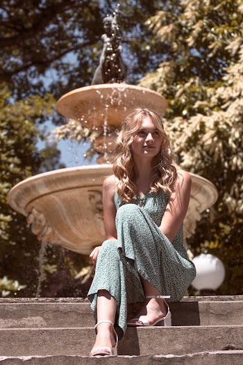 Photo of Smiling Woman in Floral Outfit Sitting on Stairs with Fountain in the Background