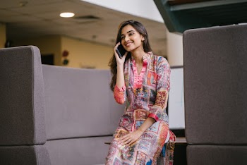 Photo of Smiling Woman in Floral Salwar Kameez Talking on Phone While Sitting on Edge of Wooden Table