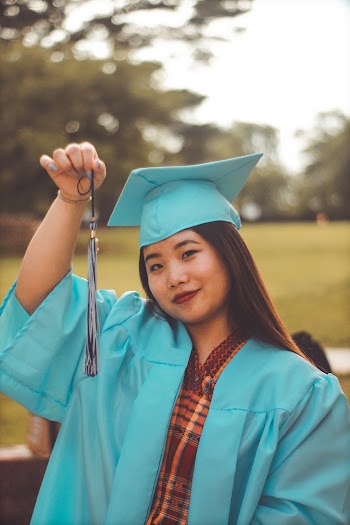 Photo of Smiling Woman in in Blue Academic Regalia Holding Up Graduation Tassel