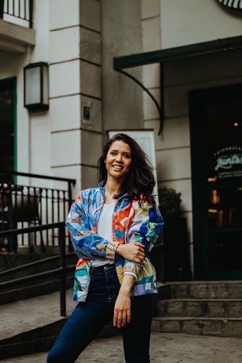 Photo of Smiling Woman in Multicolored Jacket Standing in Front of Building