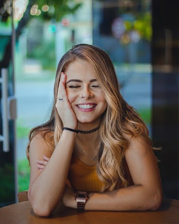 Photo of Smiling Woman in Mustard Top With Her Hands on Her Cheek and Her Eyes Closed
