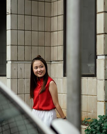 Photo of Smiling Woman in Red and White Outfit Leaning On Stone Wall Looking Away