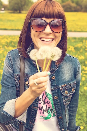Photo of Smiling Woman in Sunglasses and Blue Denim Jacket Holding Dandelions