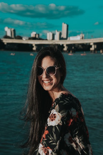 Photo of Smiling Woman in Sunglasses Posing with Body of Water in the Background