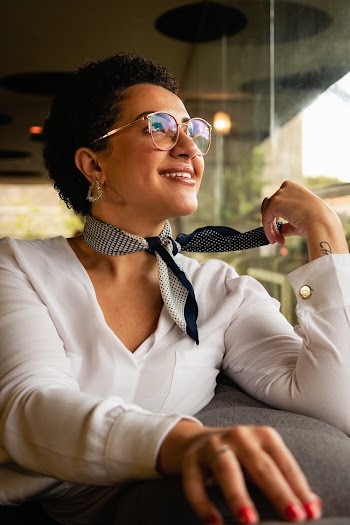 Photo of Smiling Woman in White Blouse and Glasses Posing While Sitting on Sofa Looking Away
