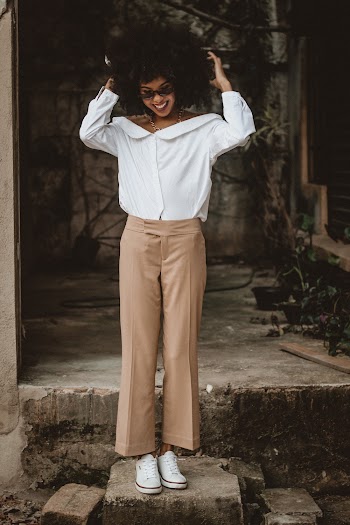 Photo of Smiling Woman in White Dress Shirt and Brown Bottoms Posing While Looking Down