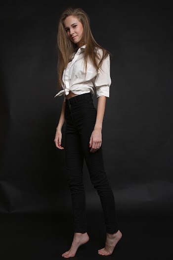 Photo of Smiling Woman in White Long-sleeved Shirt and Black Denim Jeans Standing on Her Toes