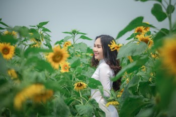Photo of Smiling Woman in White Outfit Standing in the Middle of a Sunflower Field