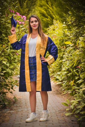Photo of Smiling Woman in White Sneakers and Blue Academic Regalia Holding Up Her Graduation Cap