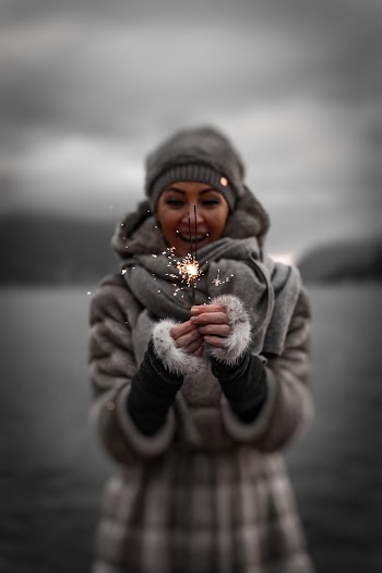 Photo of Smiling Woman in Winter Clothing Holding Sparklers