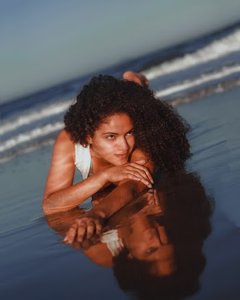 Photo of Smiling Woman Lying Down on Seashore Posing While Looking Away