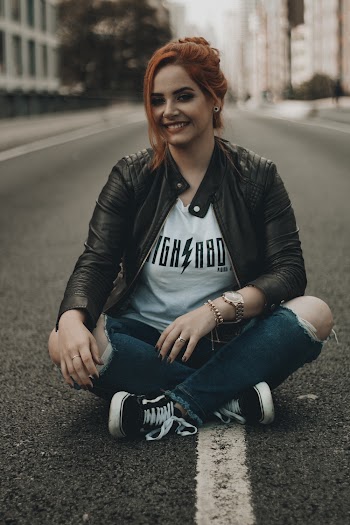 Photo of Smiling Woman Sitting in the Middle of the Road with Her Legs Crossed