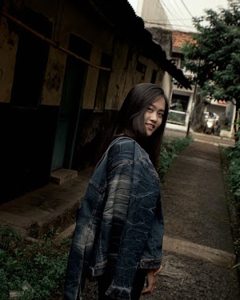 Photo of Smiling Woman Standing in an Alley Carrying Blue Denim Jacket on Shoulder