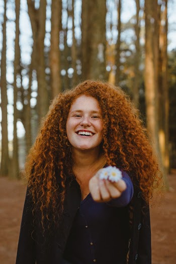Photo of Smiling Woman Standing While Holding Out White Daisy Flowers
