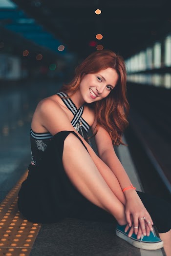 Photo of Smiling Woman Wearing Black Bottoms Sitting on Subway Platform