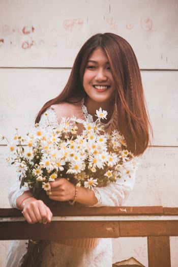 Photo of Smiling Woman Wearing White Long-sleeved Dress Holding White Daisy Bouquet