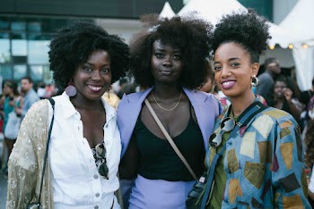 Photo of Smiling Women Posing with Crowd of People in the Background