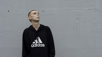Photo of Smoking Man in Black and White Adidas Hooded Standing In Front of Gray Wall