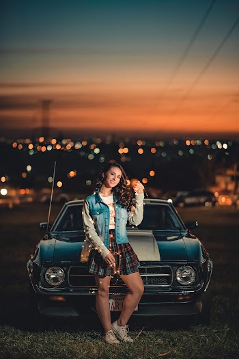Photo of Standing and Smiling Woman Holding String Lights Posing in Front of Car at Night