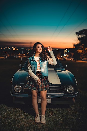 Photo of Standing and Smiling Woman Holding String Lights Posing in Front of Car at Night