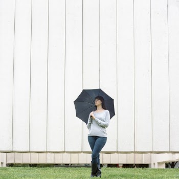 Photo of Standing Woman Holding Umbrella with Her Eyes Closed and Her Legs Crossed 