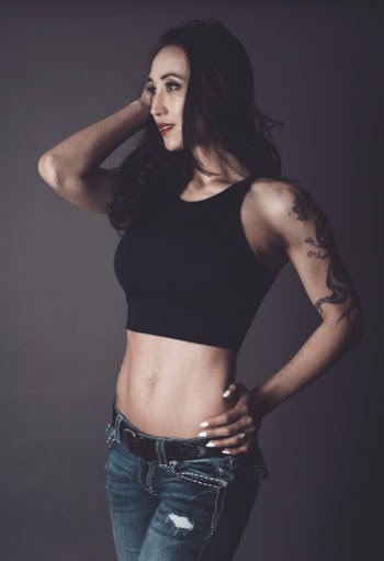 Photo of Standing Woman in Black Crop Top and Blue Jeans Posing In Front of Gray Background Looking Away