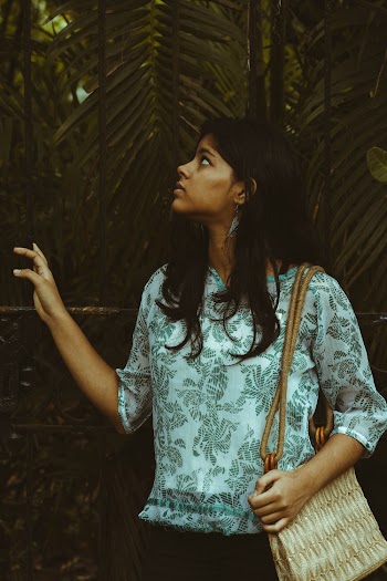 Photo of Standing Woman in Floral Shirt Looking Up at Green Leafed Plants Behind Her