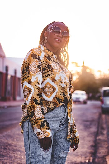 Photo of Standing Woman in Sunglasses, Floral Shirt, and Blue Jeans Posing