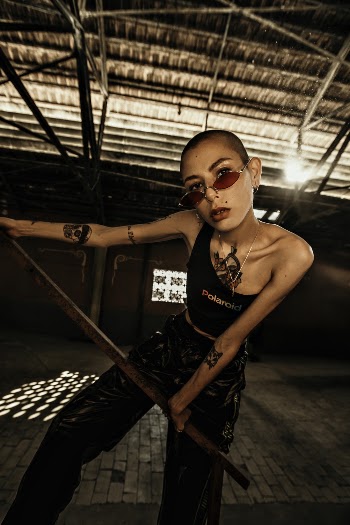 Photo of Tattooed Woman in Sunglasses and Black Outfit Leaning on Stair Railing Posing