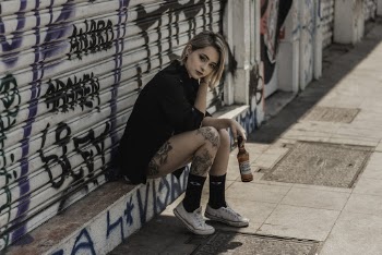 Photo of Tattooed Woman Sitting In Front of Rolling Steel Door Holding Beer Bottle