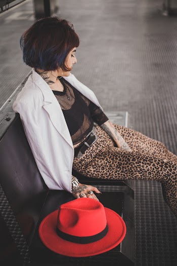 Photo of Tattooed Woman Sitting on Bench Next to Red Fedora Hat Looking Away