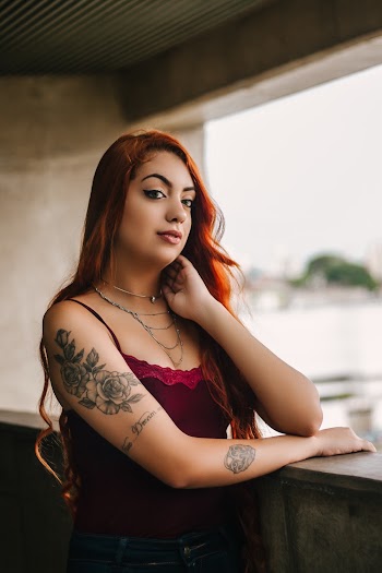 Photo of Tattooed Woman Standing and Touching Her Neck Near Stone Railing
