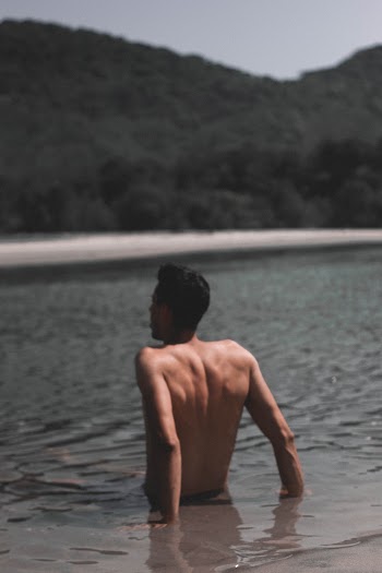 Photo Of Topless Man Sitting On Beach