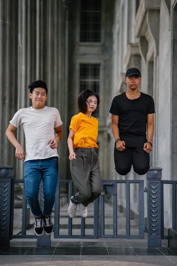 Photo of Two Men and One Woman Jumping Near Gray Gate